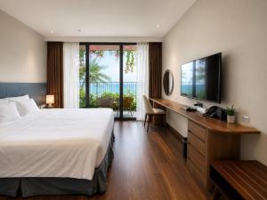 a hotel room with a bed and a desk and a television at Flamingo Cát Bà Sea Residence , Sky Villa Premier Ocean View King Bed in Hai Phong