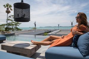 a woman sitting on a couch next to a pool at Clay Beach Samui - Beachfront Villas in Bophut