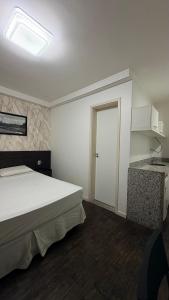 a bedroom with a white bed and a kitchen at Flat Suites Pampulha - AP 122 - Particular in Belo Horizonte