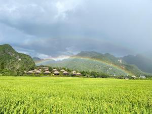 a rainbow over a green field with houses and mountains at MAI CHAU inn in Mai Châu
