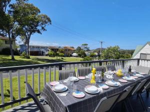 a table with plates and wine glasses on a balcony at Mollymook Beach Haven - near ocean & golf course in Mollymook