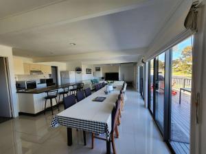 a dining room with a long table and a kitchen at Mollymook Beach Haven - near ocean & golf course in Mollymook