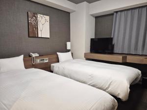 a hotel room with two beds and a flat screen tv at Hotel Route-Inn Hitachitaga in Hitachi