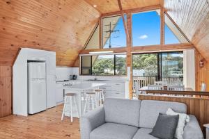 a living room with a couch and a kitchen with windows at Sea-renity in Kioloa +17 photos