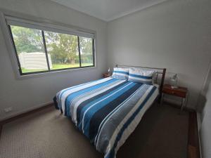 a bedroom with a bed with blue and white stripes at Bawley Backyard Haven - family retreat near beach in Bawley Point