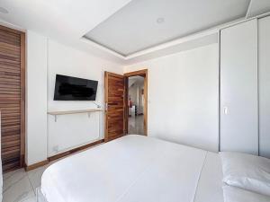 a white bedroom with a large bed and a flat screen tv at Les Sables Roses Appartement in Flic-en-Flac
