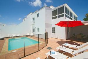 um pátio com uma piscina e um guarda-sol vermelho em Villa Webb em Puerto del Carmen