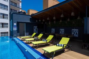a pool with green lounge chairs next to a building at Mira Heights Suites & Conferencing Mombasa in Mombasa