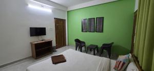 a room with a bed and chairs and a television at Hottel! Basera in Bhubaneshwar