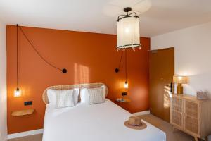 a bedroom with a white bed with an orange wall at Hôtel La Garrigue & Bar Le Perchoir in Venasque
