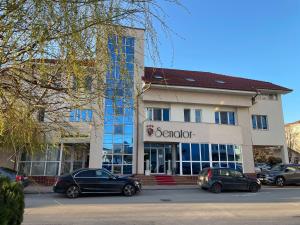 a building with cars parked in a parking lot at Hotel Senator in Slatina