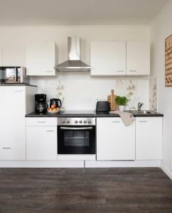 a kitchen with white cabinets and a black oven at Stilvolles Apartment mit Wintergarten, Balkon & Parkblick - VILLA KAETHE am Kurpark in Warnemünde +6 photos