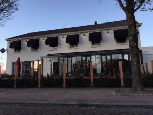 a white building with large windows and a tree at Hotel Brasserie de Kaai in Steenbergen