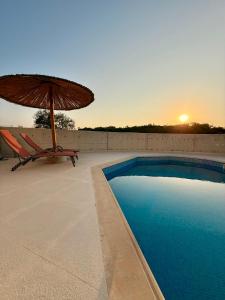 a swimming pool with an umbrella and a chair and a table at Coral Bay Garden in Peyia