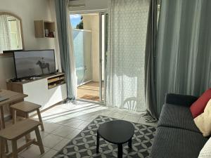 a living room with a couch and a tv and a table at Studio au calme avec piscine, face golf, parking gratuit, tout à pied à 10mn centre ville in Ciboure