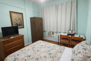 a bedroom with a bed and a desk with a television at Apto Central com Wi-Fi Rápido e Workspace in Niterói