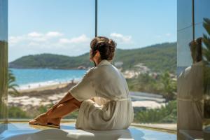 a woman sitting in a window looking out at the beach at BLESS Ibiza The Site - New Opening 2026 in Playa d'en Bossa