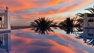 a reflection of a sunset in a pool with palm trees at Villa Mañana in Mijas +60 photos