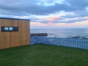 a house with a fence and a view of the ocean at Sunrise Summerhouse in Hilton of Cadboll