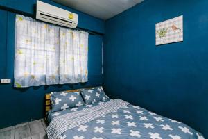 a bedroom with a blue wall with a bed and a window at Malai Place Lampang in Lampang