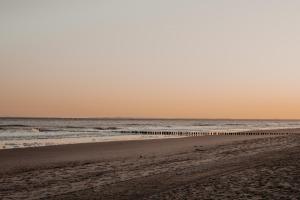 a beach at sunset with the ocean in the background at Hotel de Blanke Top in Cadzand-Bad