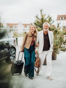 a man and a woman walking down a sidewalk with a suitcase at Hotel de Blanke Top in Cadzand-Bad