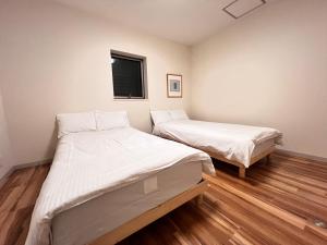 two beds in a room with wood floors and a window at 内町3階 高松中心地 広いメゾネット貸切 2ベッドルーム 最大4名 in Takamatsu