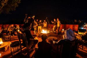 a group of people sitting around a fire at night at Luxury Sahara Desert Glamping Experience in Merzouga in Merzouga