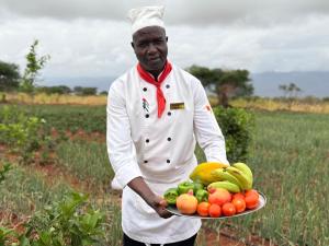 a chef holding a plate of fruit in a field at Lake Jipe Eco Lodge in Tsavo West National Park +19 photos