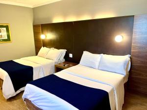two beds in a hotel room with white and blue sheets at Oasis Tower Hotel in Ribeirão Preto