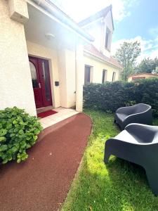 a house with a red door and two black chairs at Aux Charmes - Suites Prestige et Petit Déjeuner en chambre - Cote d Opale in Isques