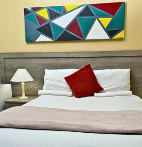 a bed with a red pillow and a painting on the wall at River-Ridge Guest House in Gaborone
