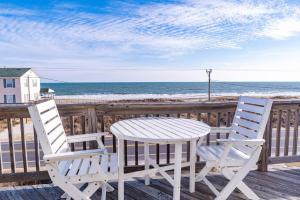two chairs and a table on a deck with the ocean at Pelican Watch - Kitty Hawk MP 3, 16 Yards to Beach, Ocean View, Pool, Hot Tub, Pool Table, Flex Stays in Kitty Hawk
