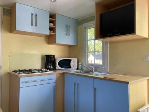 a kitchen with blue cabinets and a sink and a microwave at Camping 3 étoiles - Piscine - ccbfghc in Mamers
