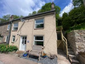 a house with a wooden bench in front of it at Carmel Cottage - Forest of Dean in Lydbrook