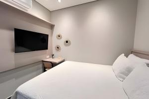 a white bedroom with a bed and a flat screen tv at Santorini Urban Studio • conforto e estilo in Londrina