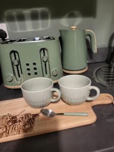 two cups on a cutting board next to a toaster at Holmleigh Place in Buxton