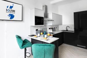 a kitchen with a white counter and green chairs at The Fountain View Apartment in Rothesay