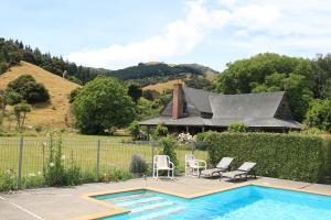 a swimming pool with two chairs and a house at Akaroa Country House in Akaroa