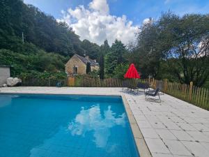 a swimming pool with a chair and a red umbrella at Ker Adèle, longère cosy au cœur d'un bois in Ploërdut