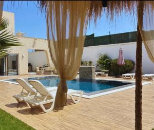 a swimming pool with two lounge chairs and a umbrella at Villa oasis in Houmt Souk