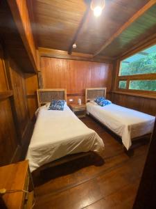 two beds in a room with wooden walls at Hotel El Abrazo del Arbol in Mindo