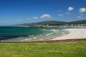 a beach with green water and mountains in the background at Duplex Playa Rapadoira con piscina in Foz