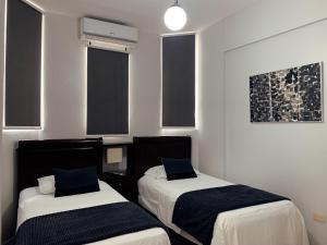 two beds in a room with white walls and windows at Hotel Libano in San Francisco de Macorís