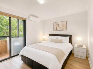 a white bedroom with a large bed and a window at Relaxing 2BR Split-Level Home in Wahroonga in Waitara