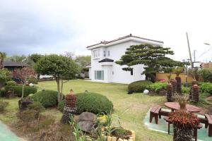 a white house with a yard with benches and trees at Maple Happy House Jeju in Jeju