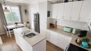 a white kitchen with a sink and a refrigerator at Beachside Cottage at Blacksmiths in Blacksmiths +10 photos