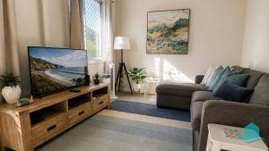 a living room with a flat screen tv on a wooden stand at Beachside Cottage at Blacksmiths in Blacksmiths