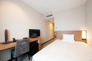 a hotel room with a bed and a desk and a tv at JR-East Hotel Mets Kitakami in Kitakami