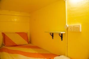 a yellow room with a bed and a shelf at Bestow Capsule Hostel in Kuala Lumpur